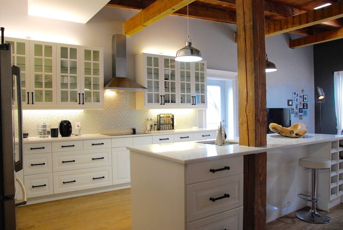 Cuisine blanche avec placards, îlot central, poutre en bois et appareils électroménagers en acier inoxydable.