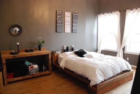 Chambre avec lit en bois, bureau et mur gris ; rideaux et linge de lit blancs.