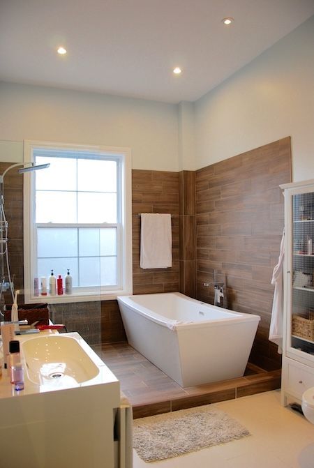Salle de bains moderne avec baignoire blanche, mur en bois et grande fenêtre.