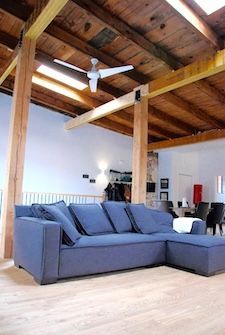Canapé d'angle bleu dans une pièce avec poutres apparentes et haut plafond ; lumineuse et aérée.
