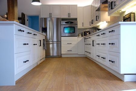 Cuisine blanche avec parquet clair, électroménagers en acier inoxydable et quincaillerie noire.