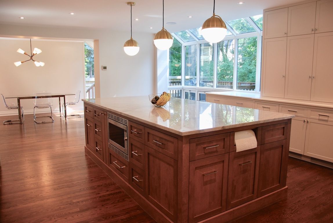 Grande cuisine avec îlot central, placards en bois et suspensions lumineuses. Une fenêtre ensoleillée donne sur un espace vert.