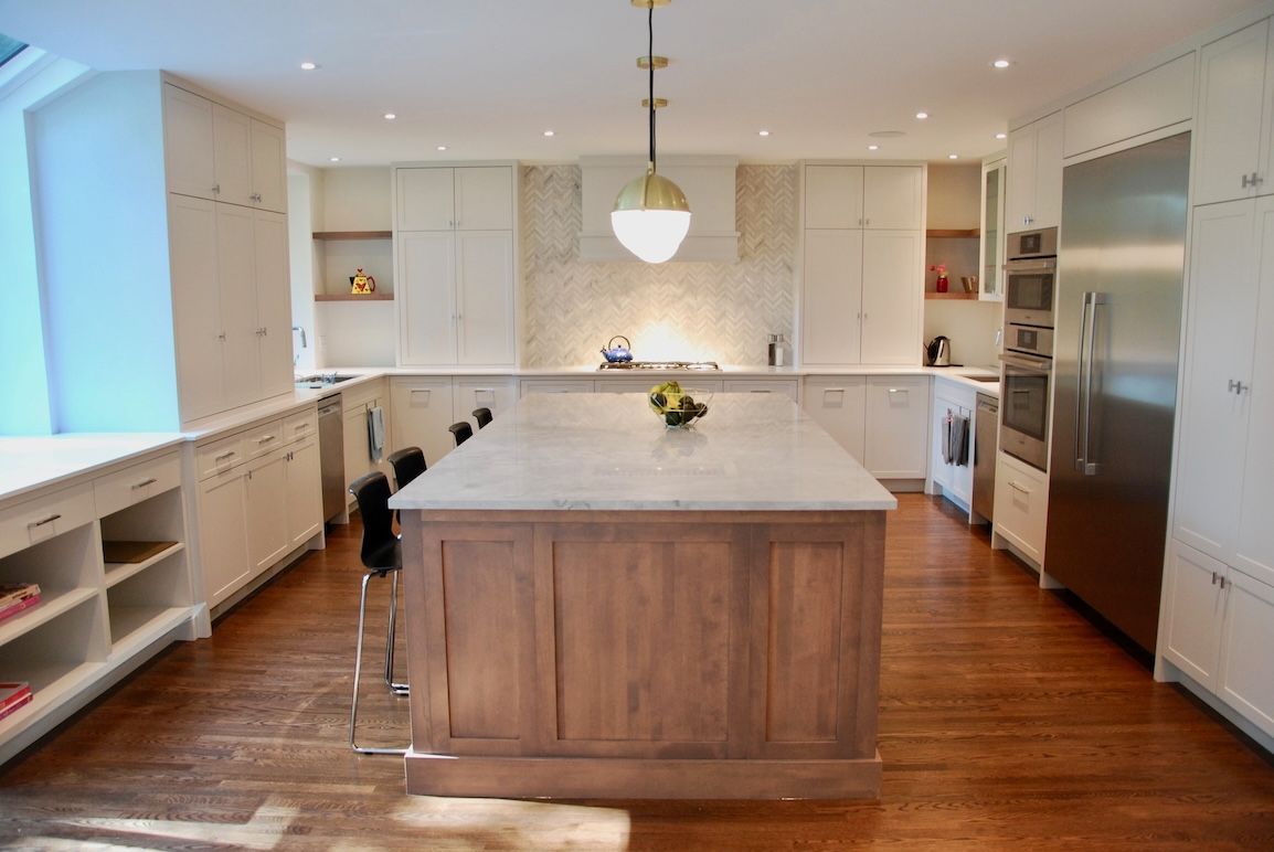 Cuisine spacieuse avec parquet, placards blancs, îlot central, réfrigérateur en inox et suspension lumineuse dorée.