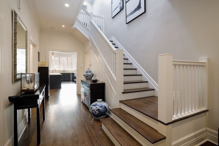 Couloir avec escalier, parquet foncé, murs blancs, meubles d'appoint noirs et bocaux décoratifs bleus et blancs.