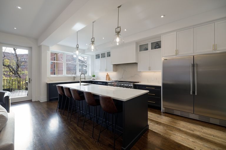 Cuisine moderne avec îlot central foncé et plans de travail clairs, réfrigérateur en acier inoxydable et suspensions lumineuses.