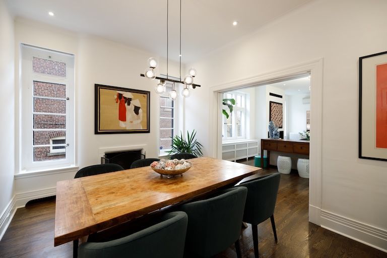 Salle à manger avec table en bois, chaises vertes, œuvres d'art et luminaire moderne.