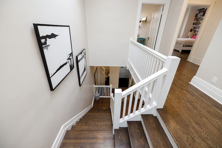 Vue de dessus d'un escalier avec une rampe blanche, des marches en bois foncé et des œuvres d'art sur un mur clair.