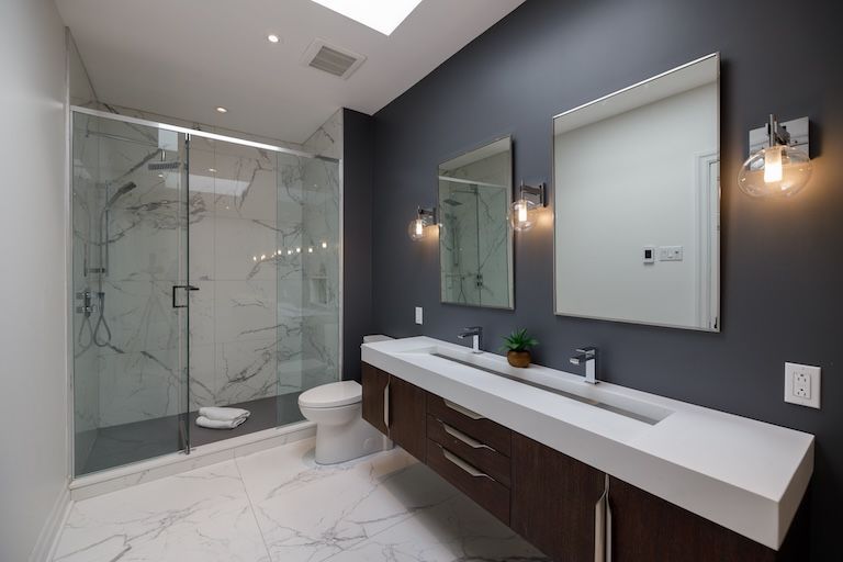 Salle de bains moderne avec douche en marbre, double vasque et mur d'accent bleu foncé.