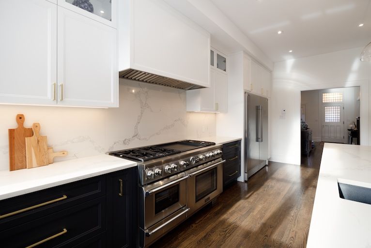 Cuisine moderne avec placards blancs et bleu marine, cuisinière et réfrigérateur en acier inoxydable et crédence en marbre.