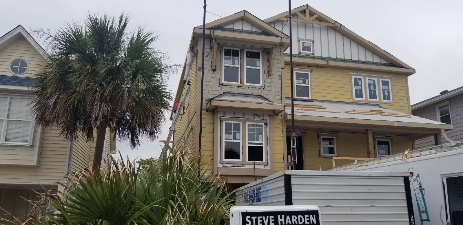 A yellow house under construction with exposed siding and scaffolding; a palm tree in front.