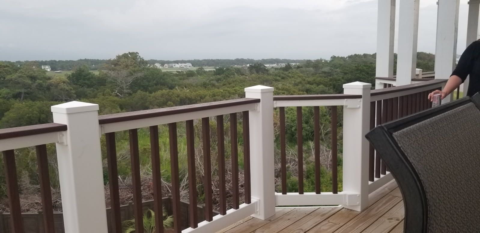 A man is standing on a deck with a view of a forest.