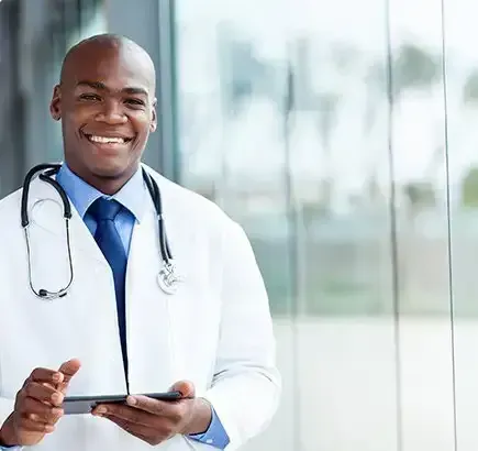 A Smiling Doctor With a Stethoscope Around His Neck is Holding a Tablet — Northern Beaches GP Superclinic in Deeragun, QLD