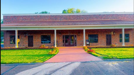 Single-story brick building with a covered entrance, red walkway, and green lawn.