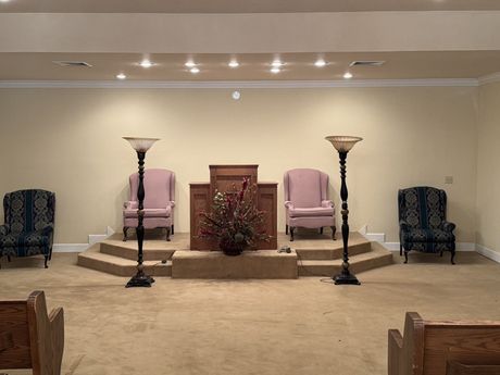 Church sanctuary with a central pulpit, floral arrangement, and chairs on a raised stage