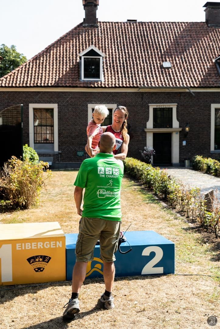 Een man in een groen shirt staat naast een podium met het nummer 2 erop.