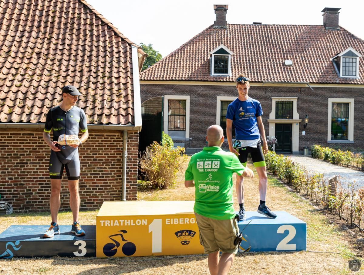 Drie mannen staan ​​op een podium voor een bakstenen gebouw.