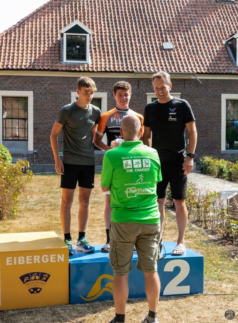 Een man in een groen shirt staat op een podium met twee andere mannen.