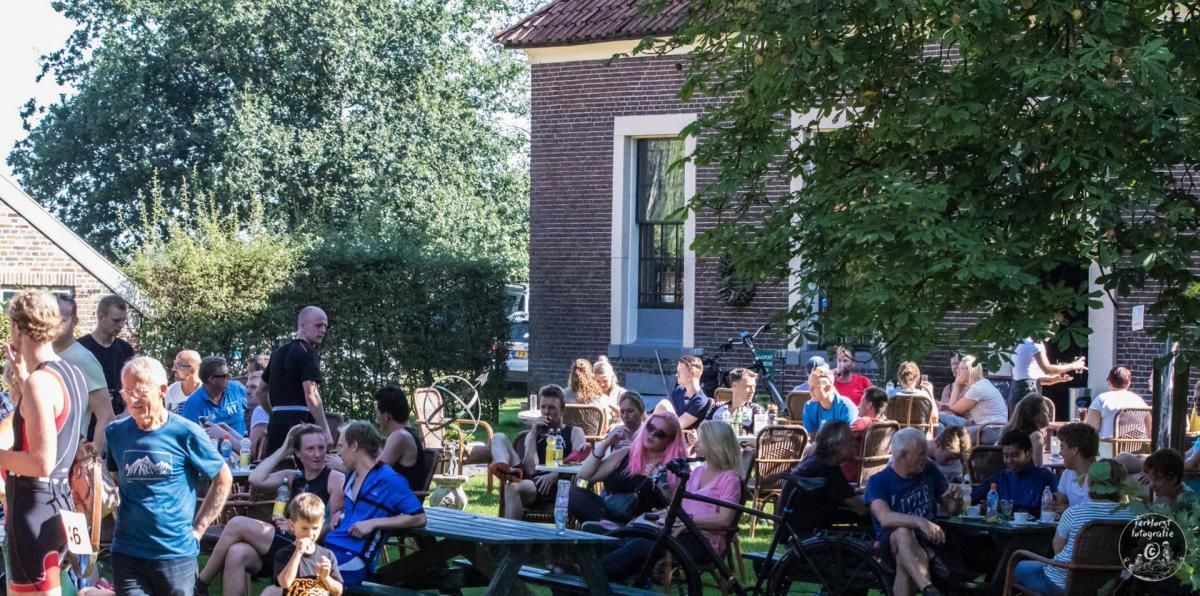 Een groep mensen zit aan tafels buiten een gebouw.