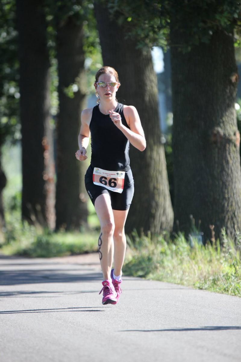 Een vrouw rent over de weg met het nummer 66 op haar startnummer.