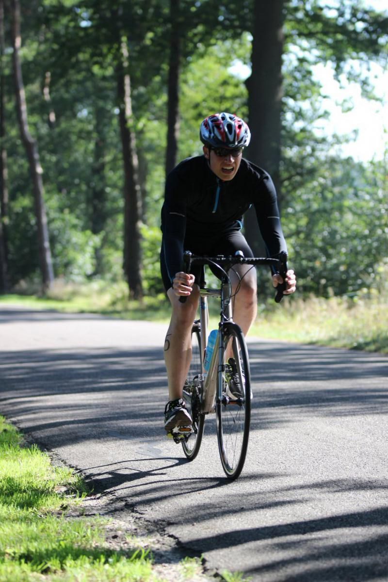Een man met een helm rijdt op een fiets over de weg.