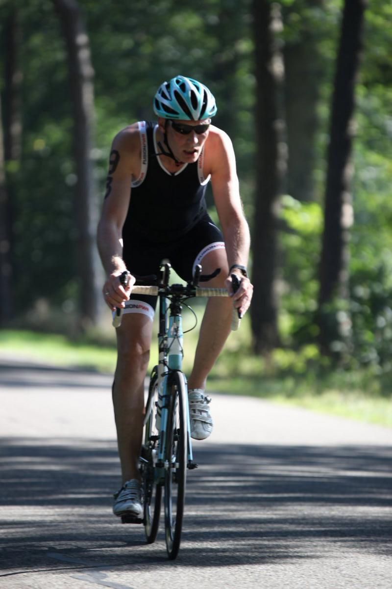 Een man met een helm rijdt op een fiets over de weg.