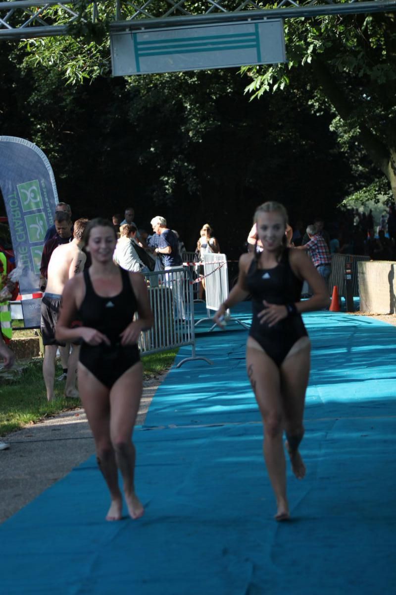 Twee vrouwen in badpakken rennen over een blauwe loper.
