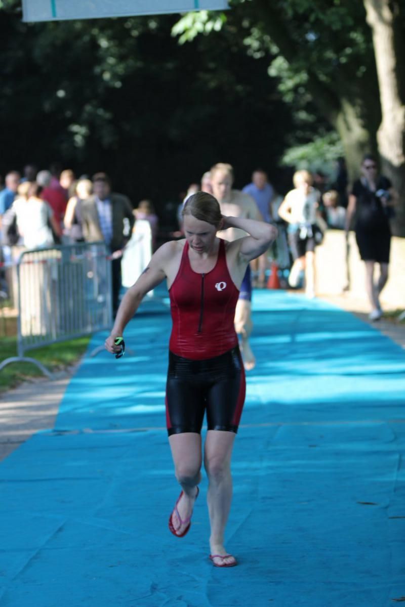Een vrouw in een rood tanktopje en zwarte shorts rent op een blauwe baan