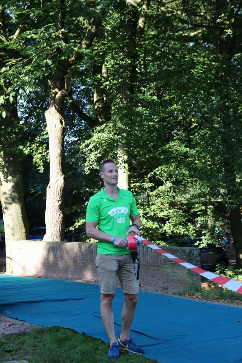 Een man in een groen shirt houdt een rood-wit lint vast.