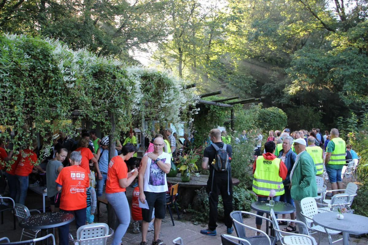 Een groep mensen staat rond tafels en stoelen in een park.