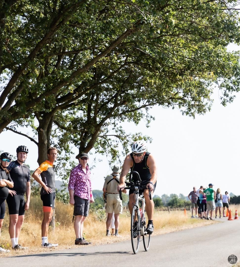 Een groep mensen kijkt naar een man die op een fiets over de weg rijdt.