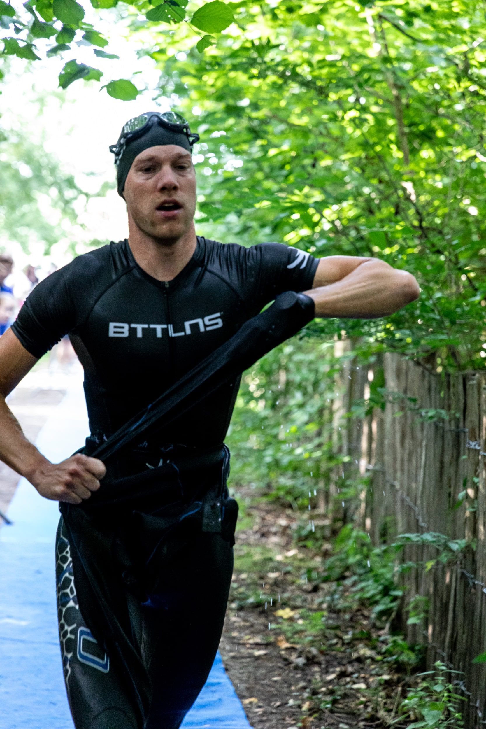 Een man in een wetsuit loopt over een pad in het bos.