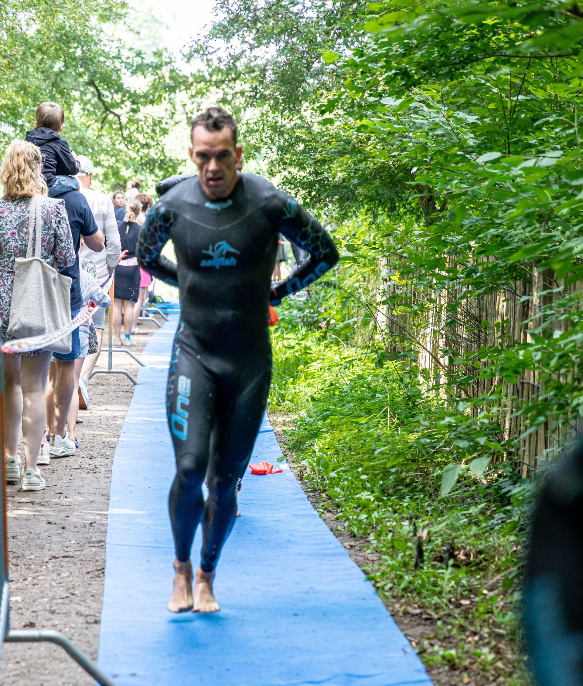 Een man in een wetsuit rent over een blauw pad.