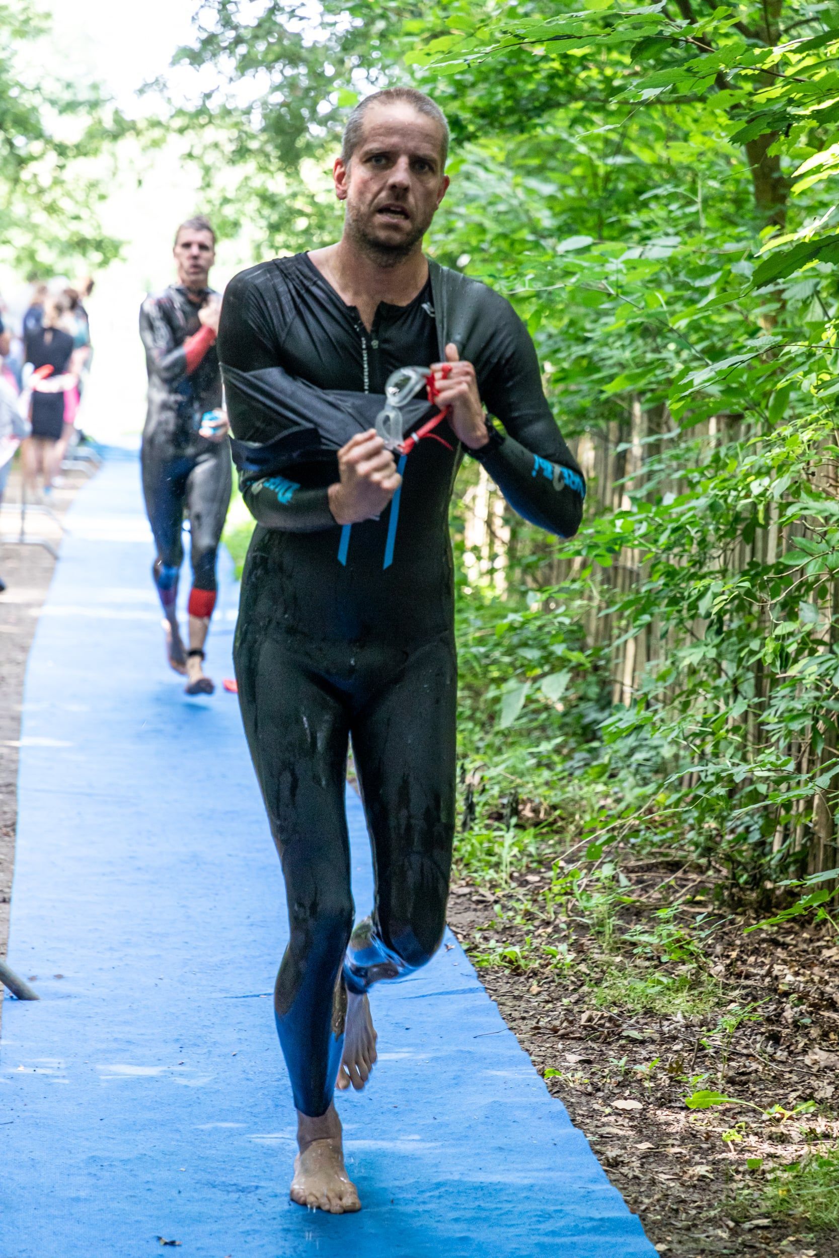 Een man in een wetsuit rent op een blauw pad.