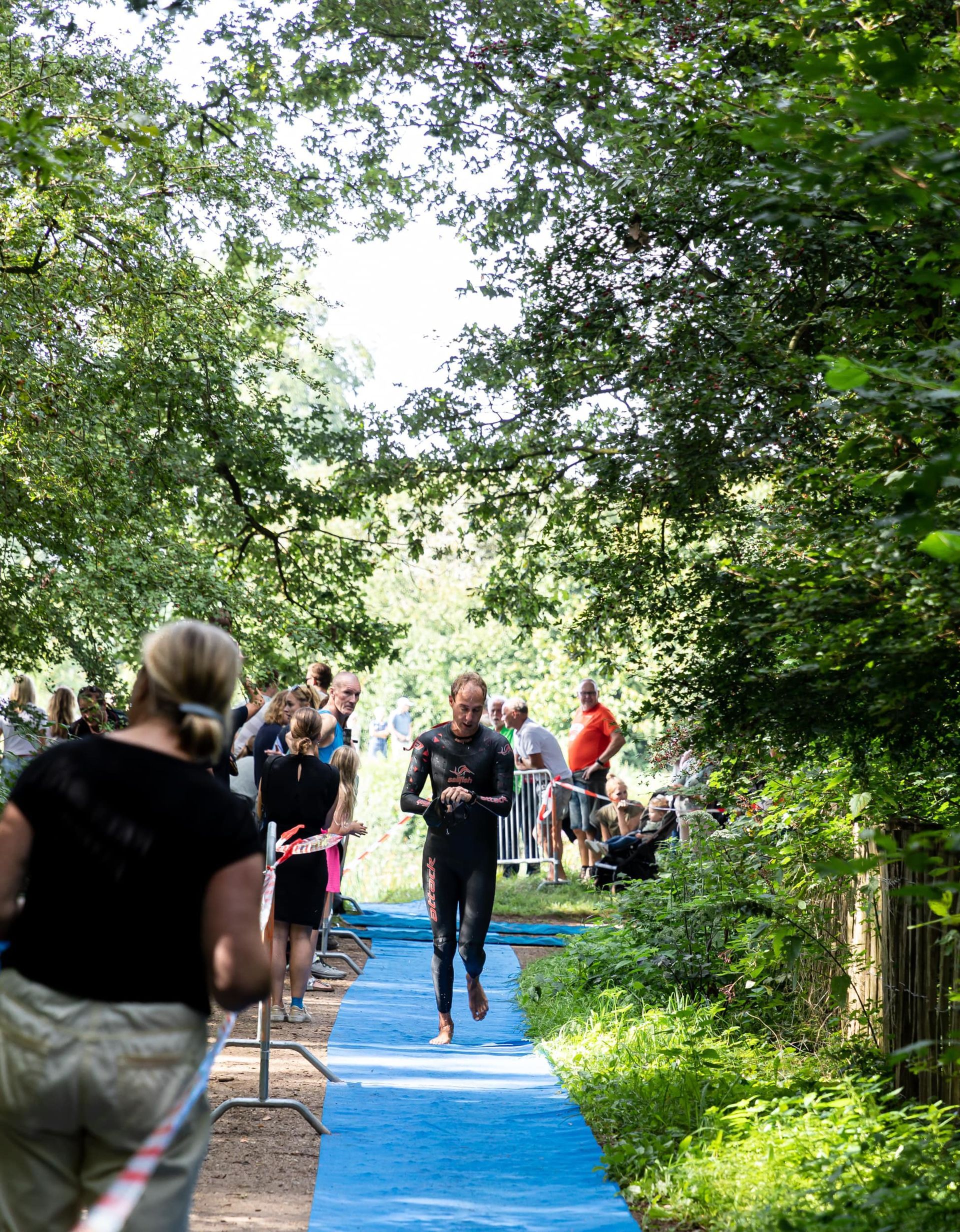 Een man in een wetsuit rent over een blauw pad in het bos.