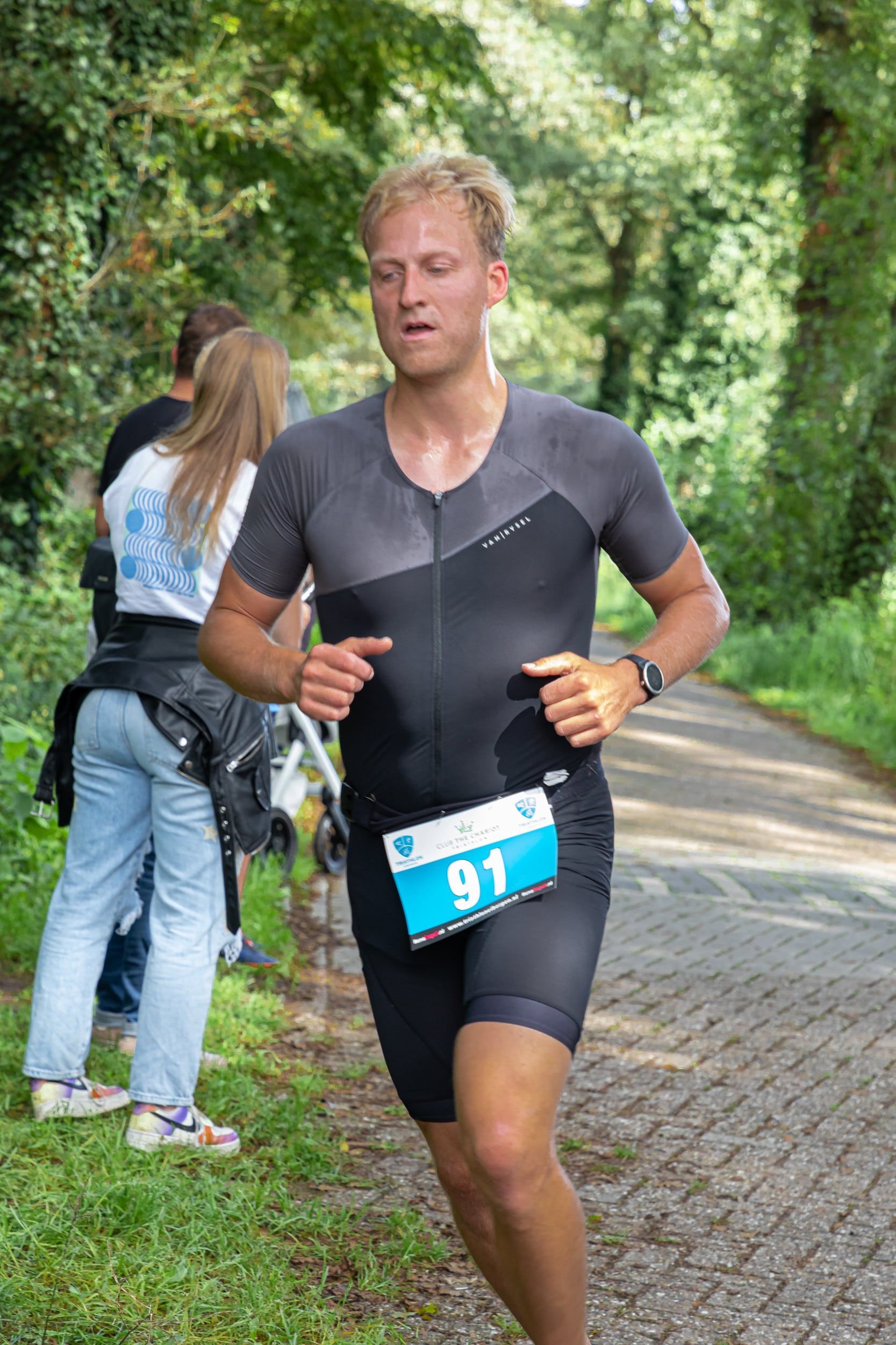 Een man in een triatlonpak rent over de weg.
