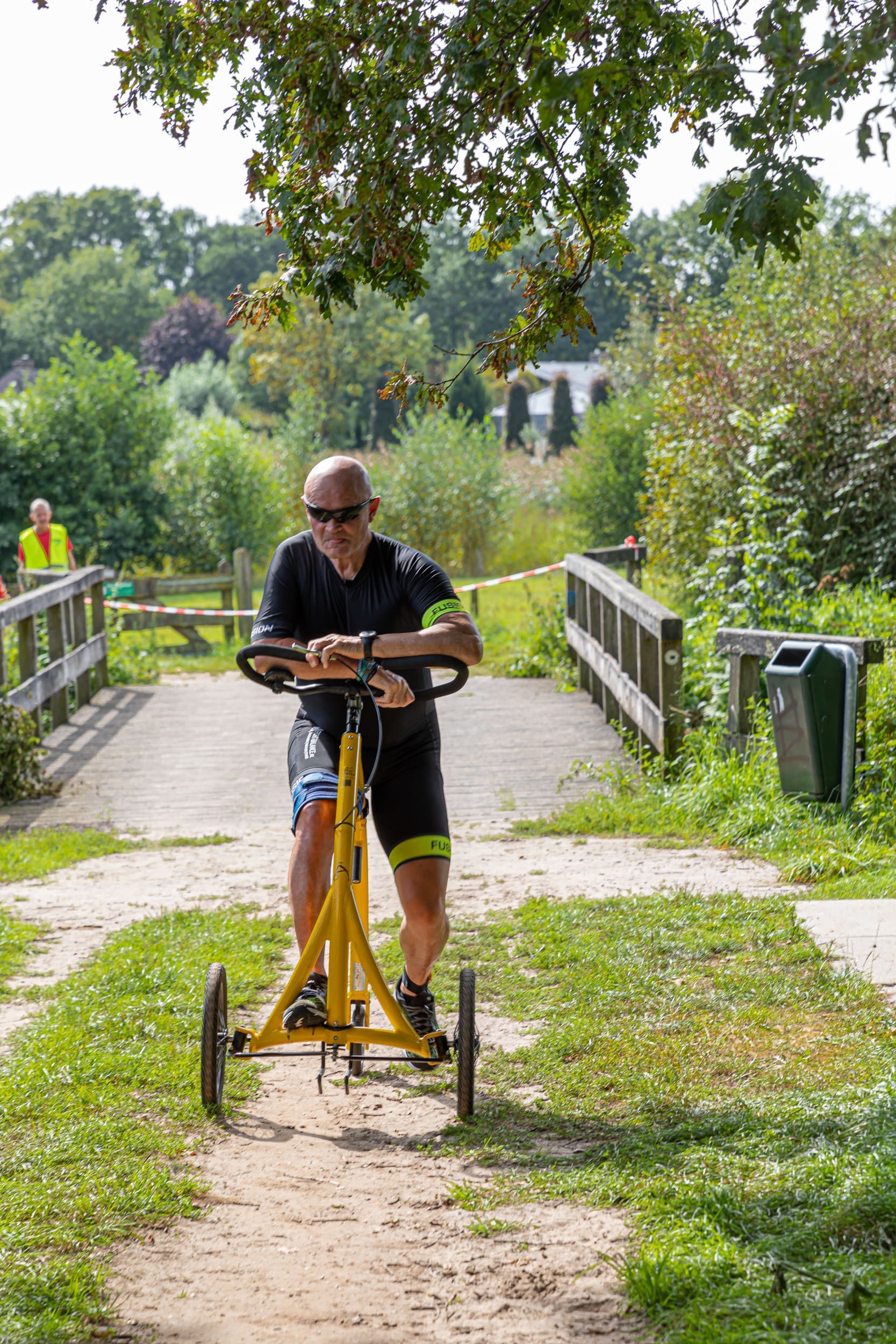Een man rijdt op een gele fiets op een onverhard pad.