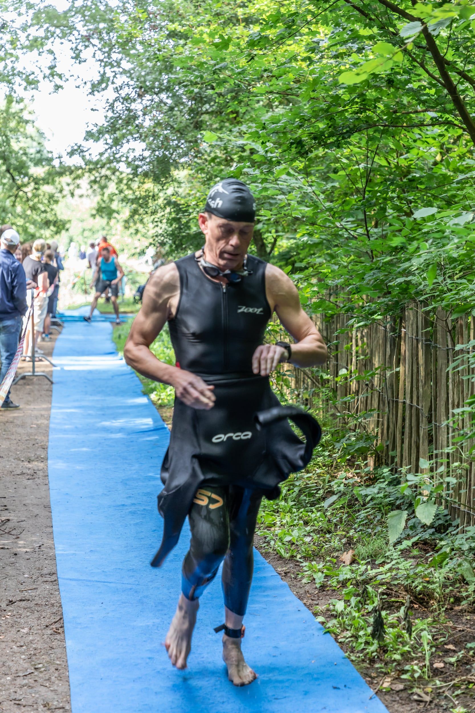 Een man in een wetsuit rent op een blauw pad in het bos.