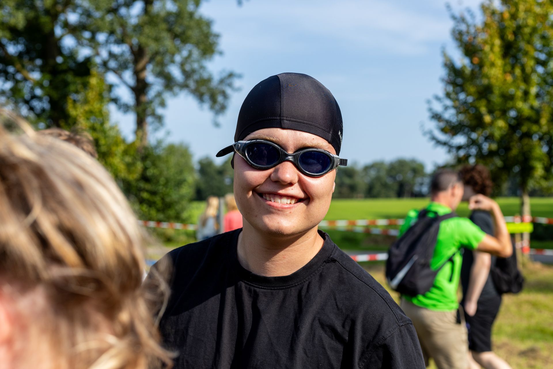 Een vrouw met een badmuts en een zonnebril lacht.