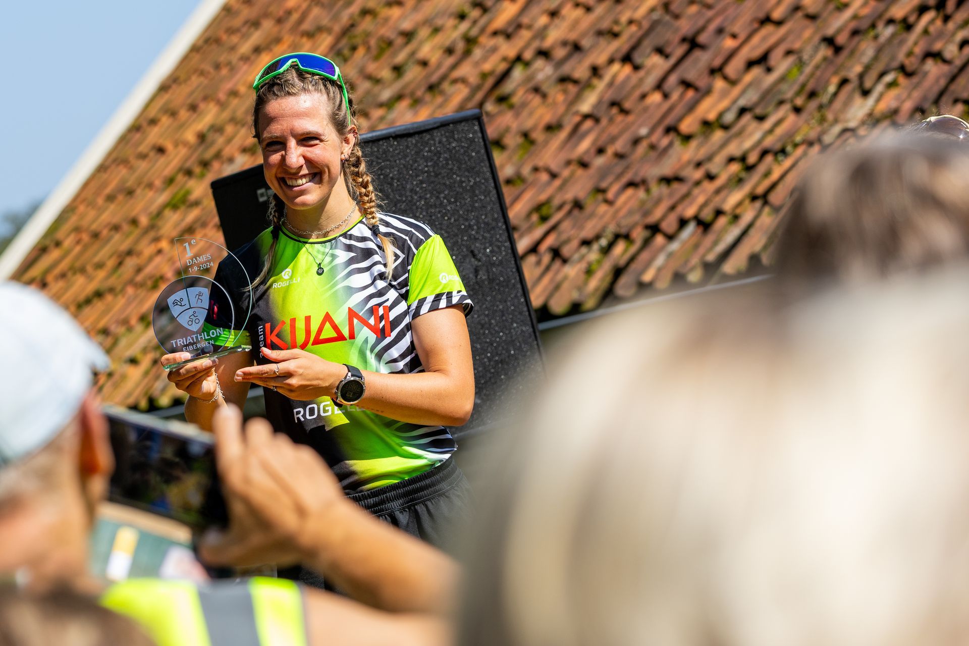 Een vrouw houdt een trofee vast voor een menigte mensen.