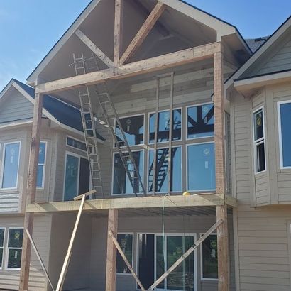 Townhouse under construction with wooden framing, ladders, and blue house wrap on the front facade