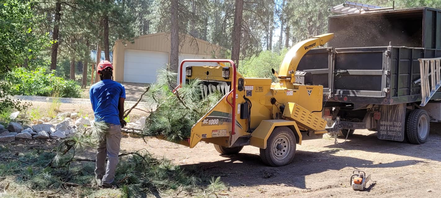 A man is standing in front of a tree chipper.