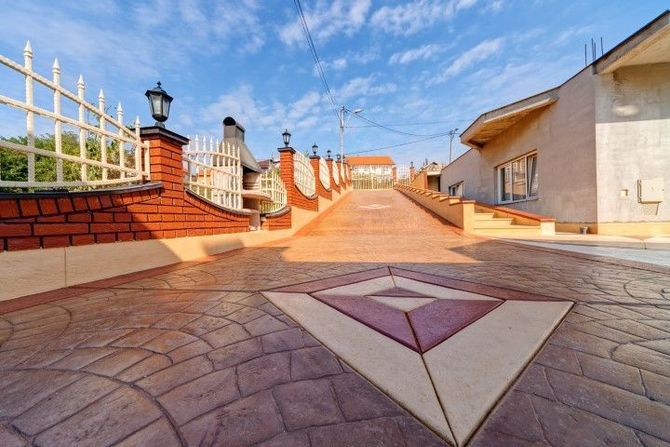 Sunlit rooftop terrace with tiled floor, white walls, brick accents, and decorative railings under a blue sky