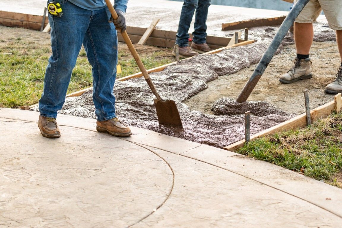 Workers pouring and smoothing wet concrete along a sidewalk edge with shovels and rakes