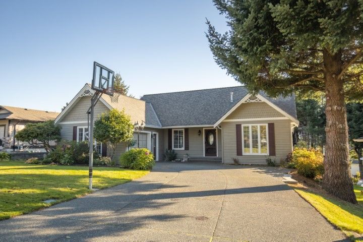 Suburban single-story house with a front porch, driveway, lawn, and basketball hoop at sunset.