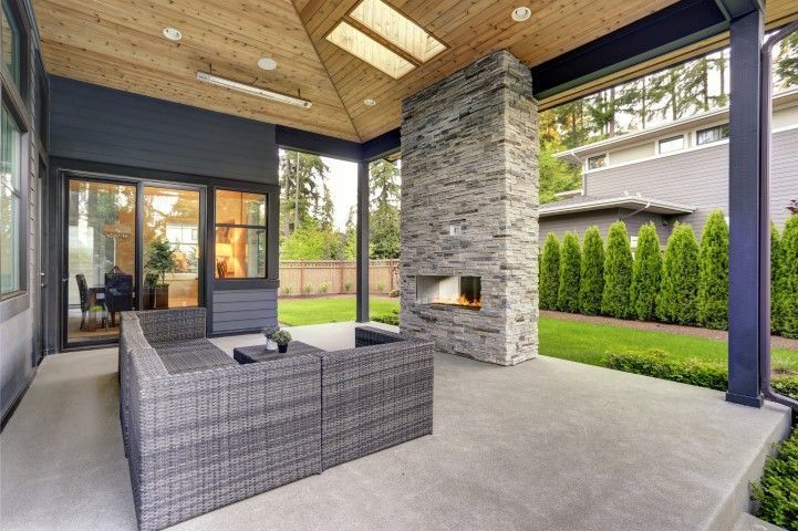 Covered patio with wicker sofa, stone fireplace, and green backyard view