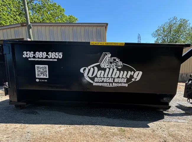 A dumpster for wallburg disposal works is parked in a gravel lot.