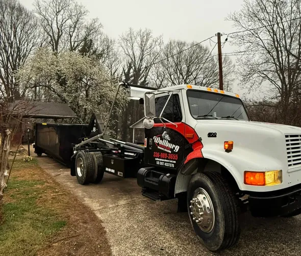 A dump truck is pulling a dumpster down a dirt road.