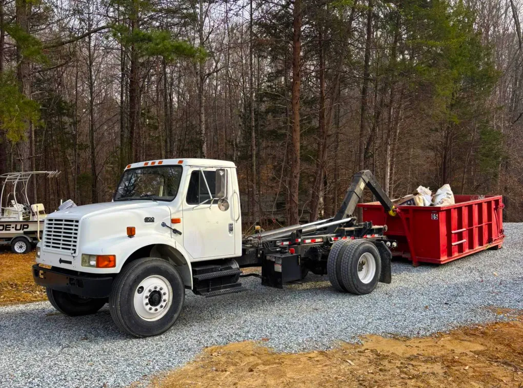 A white dump truck is pulling a red dumpster down a gravel road.