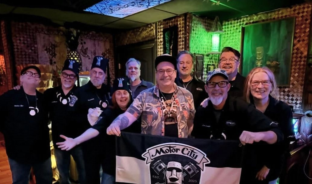 Group of people holding a flag with a Polynesian-inspired design, indoors with decorated walls.