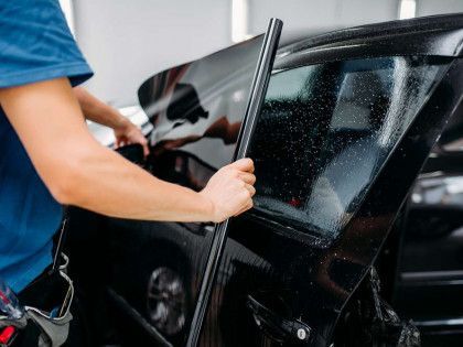 A man is applying tinted glass to a car window.